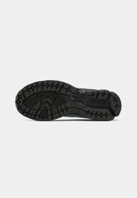 Semelle de chaussure noire avec des crampons profonds à motifs multiples conçus pour l'adhérence et la durabilité, vue par le dessous sur fond blanc.