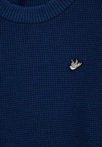 Pull texturé bleu marine avec un col côtelé, arborant un petit logo brodé en forme de main blanche sur le devant.