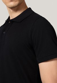 Czarna koszulka polo z kołnierzykiem, krótkimi rękawami i teksturowanym materiałem. Posiada dwa guziki i dopasowany fason z przeszytymi szwami.