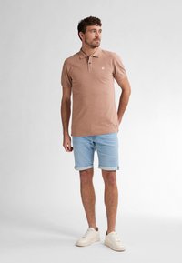 Světlé hnědé polo triko s límečkem a třemi knoflíky, v kombinaci s vyhrnutými světle modrými denimovými kraťasy a bílými teniskami.