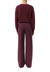 Person standing with back facing, wearing a burgundy knit sweater and matching wide-leg trousers against a white background.