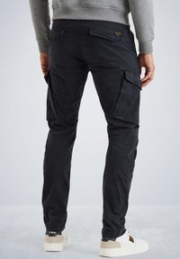 Schwarze Cargo-Hosen mit mehreren Taschen, geradem Schnitt und leichtem Glanz. Getragen mit einem hellgrauen Sweatshirt und weißen Turnschuhen.