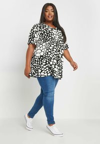 Túnica de puntos en blanco y negro con un corte holgado, combinada con jeans skinny azules y zapatillas blancas. Tejido suave y manga corta.