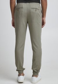 Jasnozielone spodnie z elastycznym paskiem w talii, dwoma tylnymi kieszeniami, ściągaczami na sznurek i fakturowaną tkaniną. Noszone z białymi trampkami.