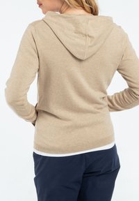 Pull à capuche beige avec une texture douce, des manches longues et un ourlet ajusté. Présente un design décontracté adapté à la superposition.