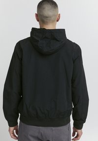 Black lightweight jacket with a hood, elastic cuffs, and hem. Smooth texture with minimal stitching detail, designed for casual wear.