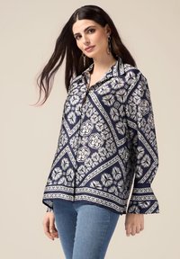 Blusa blu navy con motivi floreali bianchi, dotata di colletto, chiusura con bottoni e maniche svasate. Realizzata in tessuto leggero e morbido.