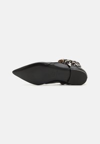 Chaussure noire à bout pointu avec une finition en cuir brillant et des accents métalliques décoratifs sur le dessus. Semelle en caoutchouc plate pour une bonne adhérence.