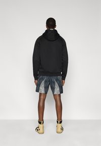 Μαύρο φούτερ με κουκούλα, σορτς με σχέδιο σε σκούρο μπλε και λευκό, και μπεζ μπότες. Τα σορτς έχουν σχέδιο φύλλου και υφή υφάσματος.