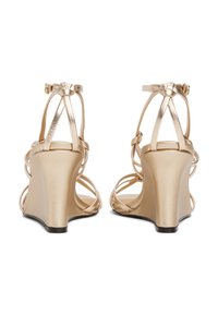 Sandales en or à talon compensé avec un design à lanières et boucle à la cheville. Fini métallique lisse et talon courbé pour plus de hauteur et de soutien.