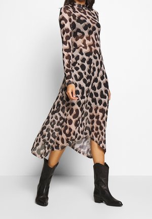 Kobieta ubrana w sukienkę midi z długim rękawem i wysokim kołnierzem w panterkę, zestawioną z czarnymi skórzanymi kozaczkami do połowy łydki, stojąca na białym tle.