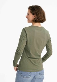 Langärmliges olivgrünes Baumwollhemd mit rundem Ausschnitt und figurbetontem Schnitt, kombiniert mit hellblauen High-Waist-Jeans.