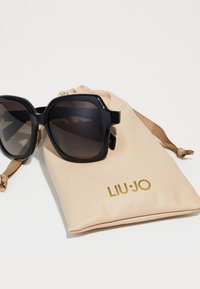 Occhiali da sole oversize neri con lenti scure e montatura quadrata; include un sacchetto beige con la scritta dorata "LIU·JO".