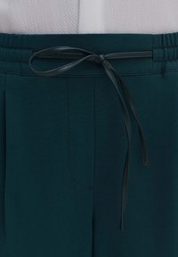 Pantalones teal con cintura elástica, que cuentan con un lazo de tela a juego en la parte delantera. Material suave con un detalle de bolsillo lateral.