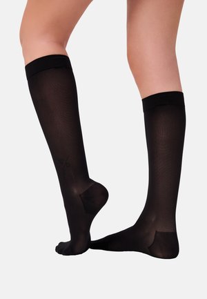 Schwarze kniehohe Socken mit glatter Textur, die ein einfarbiges Design und eine subtile gedruckte Gesichtsgraphic in der Nähe des Knöchels aufweisen.