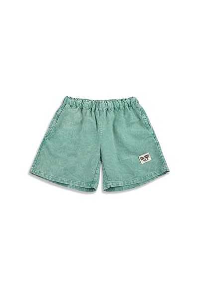 Shorts verts à taille élastique avec une petite étiquette rectangulaire blanche sur la jambe gauche indiquant "BRON CROSS SINCE 1991".