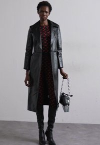 Trench coat din piele neagră peste o rochie roșie cu model. Cizme negre până la genunchi și o geantă mică cu un lanț argintiu.