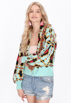 Multikleurige, gemusterde cardigan met een franjes detail; voornamelijk turquoise met rode, zwarte en gele accenten; knoopsluiting en geribbelde manchetten.