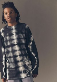 Langärmliges Schwarz-Weiß-Tie-Dye-Shirt mit Blitzgrafik-Detail an der Seite, aus weichem Stoff, mit lockerer Passform und Rundhalsausschnitt.
