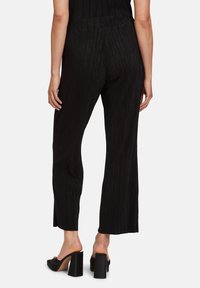 Černé žebrované kalhoty s rovnými nohavicemi, zkráceným lemem a elastickým pasem, doplněné černými otevřenými botami na blokovém podpatku.