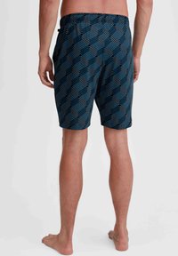 Blue patterned swim shorts with a drawstring waistband, featuring a geometric design and a soft texture. Visible skin tone and bare feet.