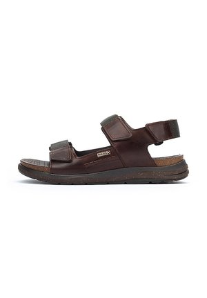 Sandale en cuir marron avec deux sangles Velcro réglables, semelle intérieure en liège, semelle en caoutchouc texturé et accents sombres contrastants.