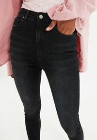 High-waisted black jeans made of denim with a slim fit. Features a front button closure and pocket; slight texture in fabric.