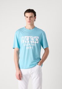 Lys blå bomull t-skjorte med stort hvitt grafisk trykk av "HUGO" og "CREATIVE DEPT." Rund hals og korte ermer.