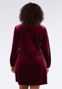 Abito in velluto borgogna con maniche lunghe, vestibilità morbida e motivo a pois bianchi. Presenta maniche arricciate e un dettaglio in corrispondenza della vita.