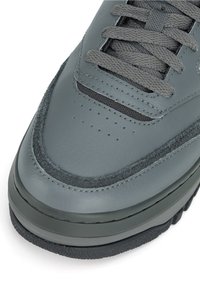 Šedá kožená teniska s hladkým zvrškom, textúrovanými detailmi, zaoblenou špičkou a sivými šnúrkami, s čiernou gumovou podrážkou.