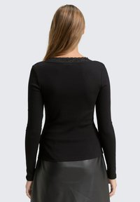 Schwarzes Langarmoberteil aus geripptem Stoff, mit einer Spitzenverzierung am Ausschnitt, figurbetontem Design und geradem Schnitt am Saum.