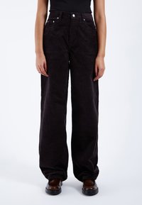 Pantalones de pana negros de pierna ancha con cintura alta, que cuentan con bolsillos frontales, cierre de botón y sutiles costillas verticales en la textura de la tela.