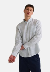 Chemise à rayures en tissu léger ; dotée d'une poche poitrine, d'un col et de manches retroussées dans des tons de bleu clair et blanc.