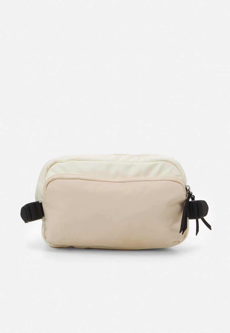 Borsa a tracolla rettangolare realizzata in morbido tessuto color crema e beige. Presenta una zip superiore, dettagli in metallo nero e una tracolla laterale regolabile.
