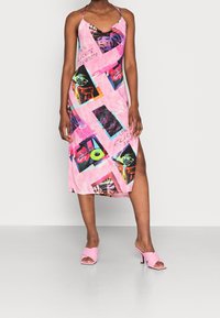 Robe midi sans manches rose avec des imprimés graphiques en couleurs contrastées, dotée d'une fente sur le côté. Associée à des mules à talons rose clair.
