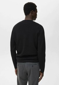 Schwarzer gestrickter Pullover mit Rundhalsausschnitt und glatter Textur. Getragen mit grauen, taillierten Hosen, von hinten betrachtet.