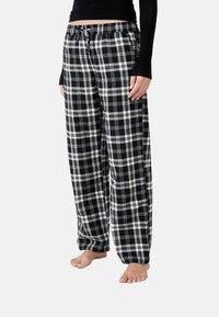 Pantalones de pijama de cuadros en blanco y negro con cintura elástica y cordón, que presentan un corte holgado y una textura de tela suave.