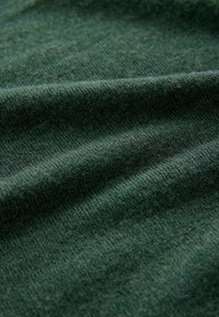 Tela de color verde oscuro con una textura suave, que muestra un sutil patrón de punto y suaves pliegues. El color es uniforme en toda su extensión.