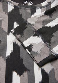 Korte mouwen shirt in zwart, grijs en wit met een geometrisch penseelstrekenpatroon. Gemaakt van zachte, rekbare stof met een ronde halslijn.