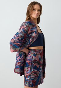 Mehrfarbiger gemusterter Kimono mit weiten Ärmeln, der in Rot-, Blau- und Grüntönen gestaltet ist. Kombiniert mit einem passenden gemusterten Rock. Sanfte Textur.