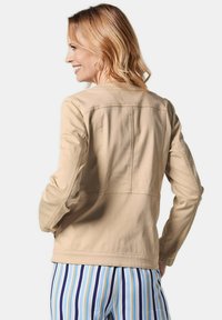 Beige jas met een rechte snit en zichtbare naden, met lange mouwen en een ronde kraag, gecombineerd met gestreepte broek in blauw en wit.