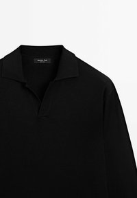 Sort polo-shirt med klassisk krave, der har en klap med en lille åbning. Fremstillet af blødt stof med minimal sømdetaljering og uden mønstre.
