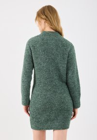 Grønn teksturert kjole i strikk, lange ermer og h�øy hals, tettsittende silhuett, mykt stoff med en dunete finish. Ingen synlige mønstre eller detaljer.