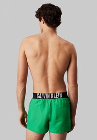 Pantaloni da nuoto verdi con una fascia in vita nera con il logo Calvin Klein, dotati di una tasca posteriore e un tessuto liscio e leggero.