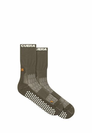 Paire de chaussettes antidérapantes vert foncé avec motifs hexagonaux et points blancs antidérapants sous les semelles, avec des détails de texte blancs et orange.