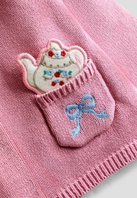 Rosa stickad tyg som visar en ficka med broderad tekanna och blommor, accentuerad av en ljusblå rosett vid fickans kant.