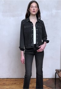 Black denim jacket with stone accents, button-down front, and two chest pockets, paired with fitted black flared jeans and a white top.