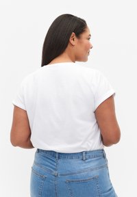 Camiseta de algodón blanca con mangas cortas enrolladas, que presenta un cuello redondo y un corte relajado. Combinada con vaqueros de mezclilla azul de cintura alta.