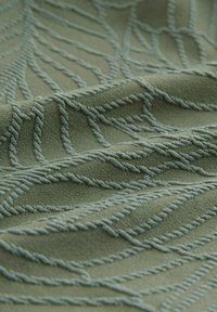 Material texturat într-o nuanță verde estompată, decorat cu modele în relief ce imită frunze într-o nuanță mai deschisă, evidențiind un design țesut moale.