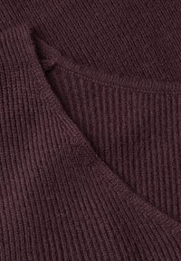Gros plan d’un tissu tricoté côtelé doux de couleur violet profond, montrant des plis superposés et de fines textures détaillées.